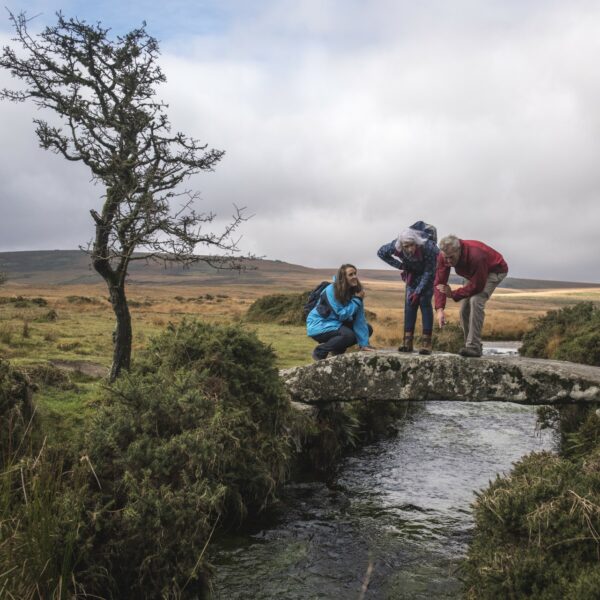 people walking over a small stone bridge during a hike
